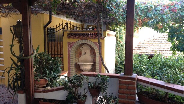 Une cour avec un mur jaune, une fontaine en briques et des plantes en pot.