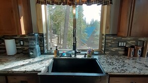 Una cocina con un lavamanos, armarios de madera, un reloj y una ventana con vistas a árboles.