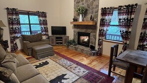 A cozy living room with a stone fireplace, a ceiling fan, and a TV. - Little Bear Cove in the Enchanted Valley of Young Harris Ga (Young Harris)