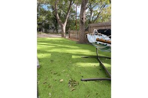 Relax in a serene outdoor space with a hammock suspended between trees, surrounded by a lush lawn and a wooden fence.