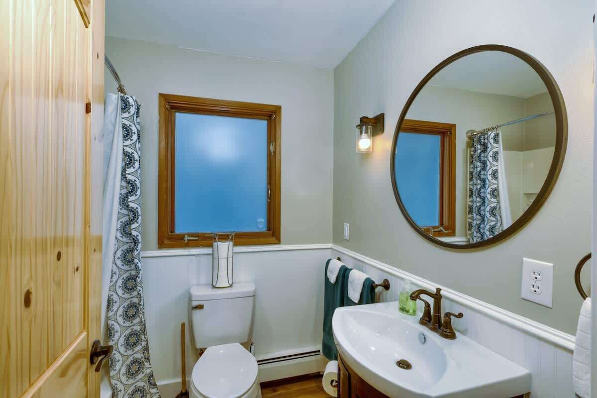 Une salle de bain avec des toilettes, un lavabo, un miroir et une fenêtre.