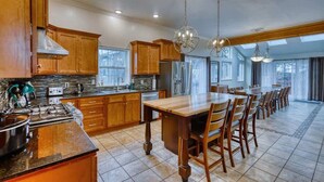 A kitchen with wooden cabinets, a granite countertop, a large island, and a dining area with chairs. - Grandeur Gathering Luxurious retreat with hot tub (Kodiak)