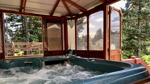 A hot tub with a wooden deck and glass walls, surrounded by trees. - Grandeur Gathering Luxurious retreat with hot tub (Kodiak)