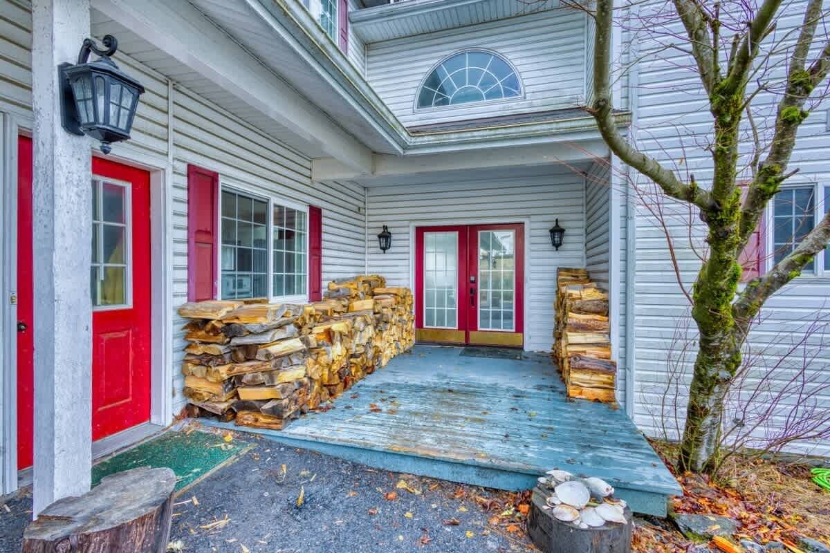 Une maison avec un porche, des portes rouges et une pile de bois de chauffage.