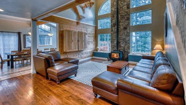 A spacious living room with a stone fireplace, leather sofas, and large windows. - Grandeur Gathering Luxurious retreat with hot tub (Kodiak)