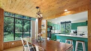A wooden interior with a dining table, chairs, and a kitchen area with green cabinets. - Combined Sequim · Spacious Farmhouse & Vintage Trailer on 5 Acres (Sequim)