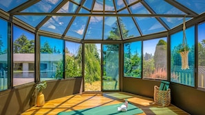 A sunlit room with large windows, a yoga mat, a small plant, and a basket. - Combined Sequim · Spacious Farmhouse & Vintage Trailer on 5 Acres (Sequim)