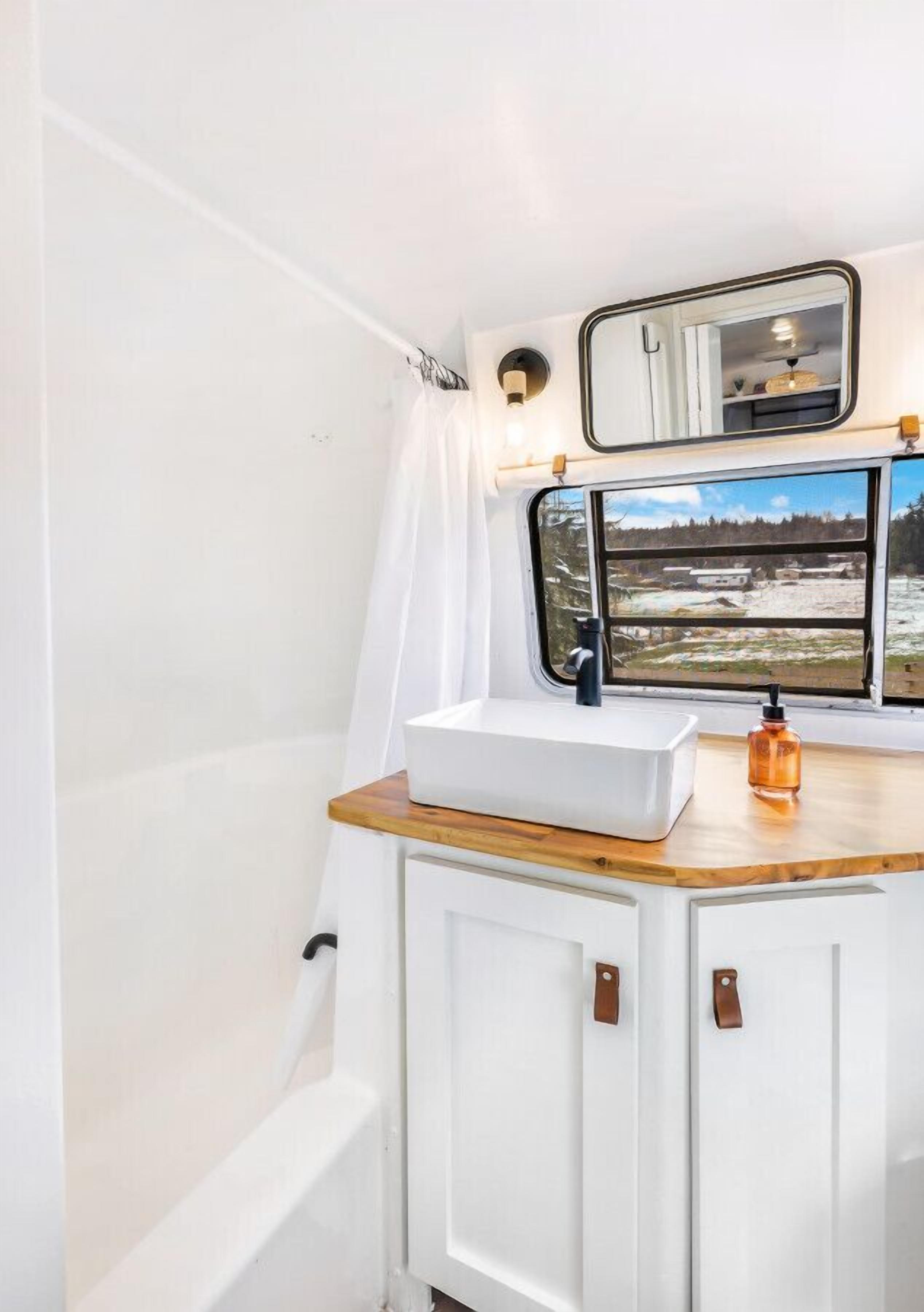 Un baño con lavamanos blanco, encimera de madera y ventana con vistas al paisaje.