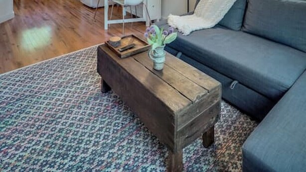A modern living room with a sofa, coffee table, and a dining area with a kitchen in the background. - Modern, Cozy Urban Homestead w/ Loft (Shoreline)