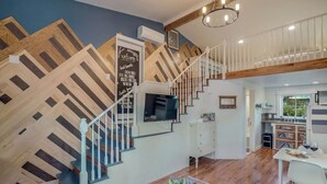 A spacious living area with a wooden staircase, a flat-screen TV mounted on the wall, and a dining area with a table and chairs. - Modern, Cozy Urban Homestead w/ Loft (Shoreline)