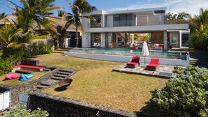 Una casa moderna de dos pisos con piscina, mobiliario exterior y jardines tropicales.
