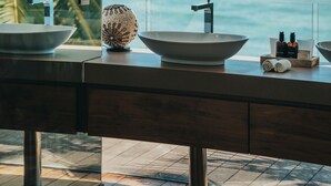 Un baño con un amplio ventanal con vistas al océano, que incluye dos lavamanos y un jarrón decorativo.