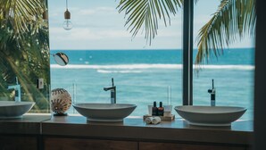 Un baño con tres lavamanos tipo isla, una concha decorativa y vistas al océano.