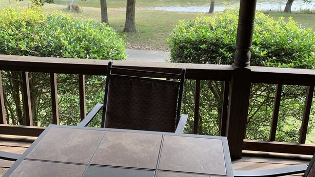 Un espace extérieur abrité, doté d’une table et de chaises, qui offre une vue sur un lac et des arbres.