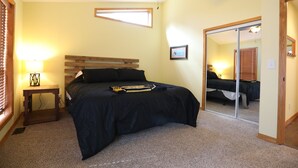 Une chambre à coucher comprenant un lit, une table de chevet, un ventilateur de plafond, une fenêtre et un miroir.