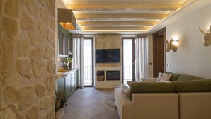 A cozy living room with a stone wall, a green sofa, a flat-screen TV, and a fireplace. - Alpujarras | Palatine Concept Suites | Luxury Apartments in Granada Center (Granada)