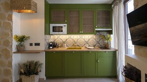 A kitchen with green cabinets, a microwave, and a sink. There are baskets with flowers and a stone wall. - Alpujarras | Palatine Concept Suites | Luxury Apartments in Granada Center (Granada)