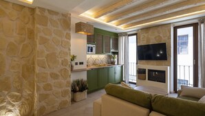 A modern living area with stone walls, a green kitchen, and a flat-screen TV mounted on the wall. - Alpujarras | Palatine Concept Suites | Luxury Apartments in Granada Center (Granada)