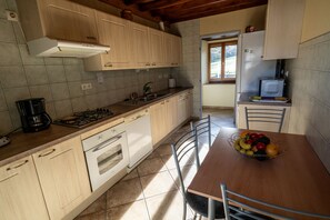 Una cocina con armarios de madera, una estufa a gas, un microondas y una mesa de comedor con sillas.