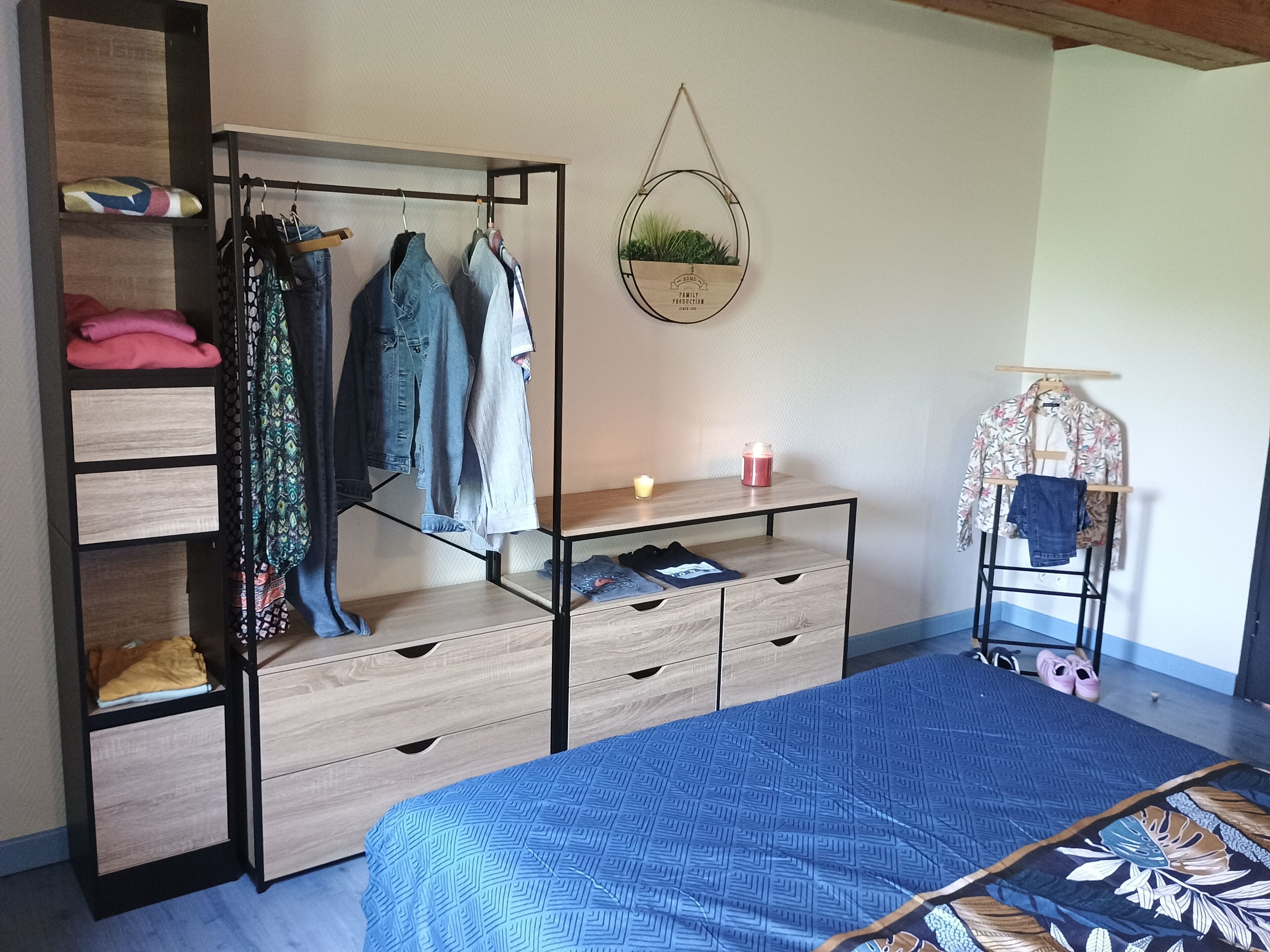A bedroom with a bed, a wardrobe, a small table with a candle, and a hanging plant.