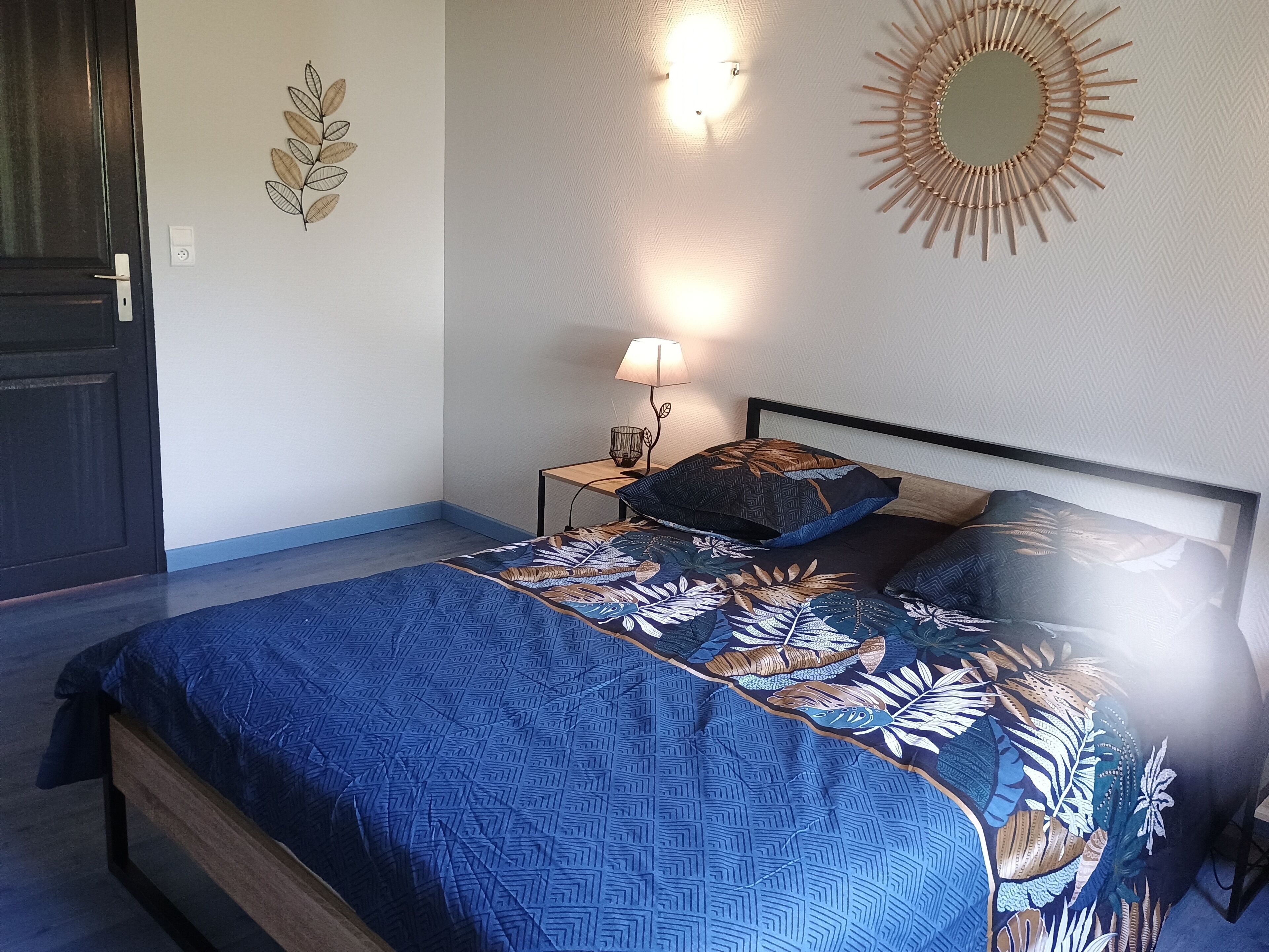 A bedroom with a bed, a nightstand, a lamp, a wall decoration, and a door.