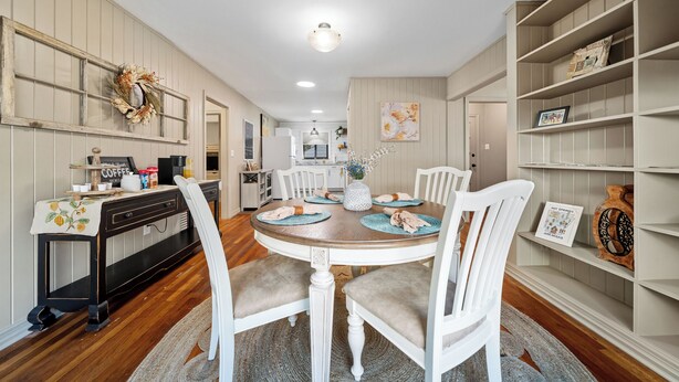 A dining area with a round table, white chairs, and a bookshelf.