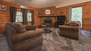 A log cabin interior with two sofas, a fireplace, and a television.