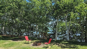 Un espacio al aire libre con césped, dos sillas rojas y un hogar para la chimenea.