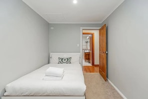 A small, single-bed room with a wooden door leading to a bathroom. - Tranquil 4 Bedroom Cottage in Olinda (Olinda)