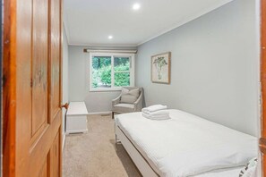 A bedroom with a single bed, a small bedside table, a chair, a window, and a door. - Tranquil 4 Bedroom Cottage in Olinda (Olinda)