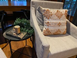 A cozy seating area with a cushioned armchair, a small round table with a book and a mug, and a decorative pillow. - Tranquil 4 Bedroom Cottage in Olinda (Olinda)