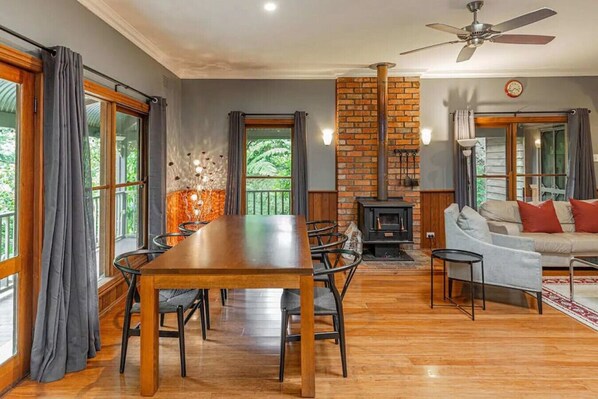A cozy living room with a fireplace, a dining area with a wooden table and chairs, and a sofa. - Tranquil 4 Bedroom Cottage in Olinda (Olinda)
