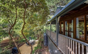 A covered outdoor area with a wooden deck, a grill, and a table with chairs.