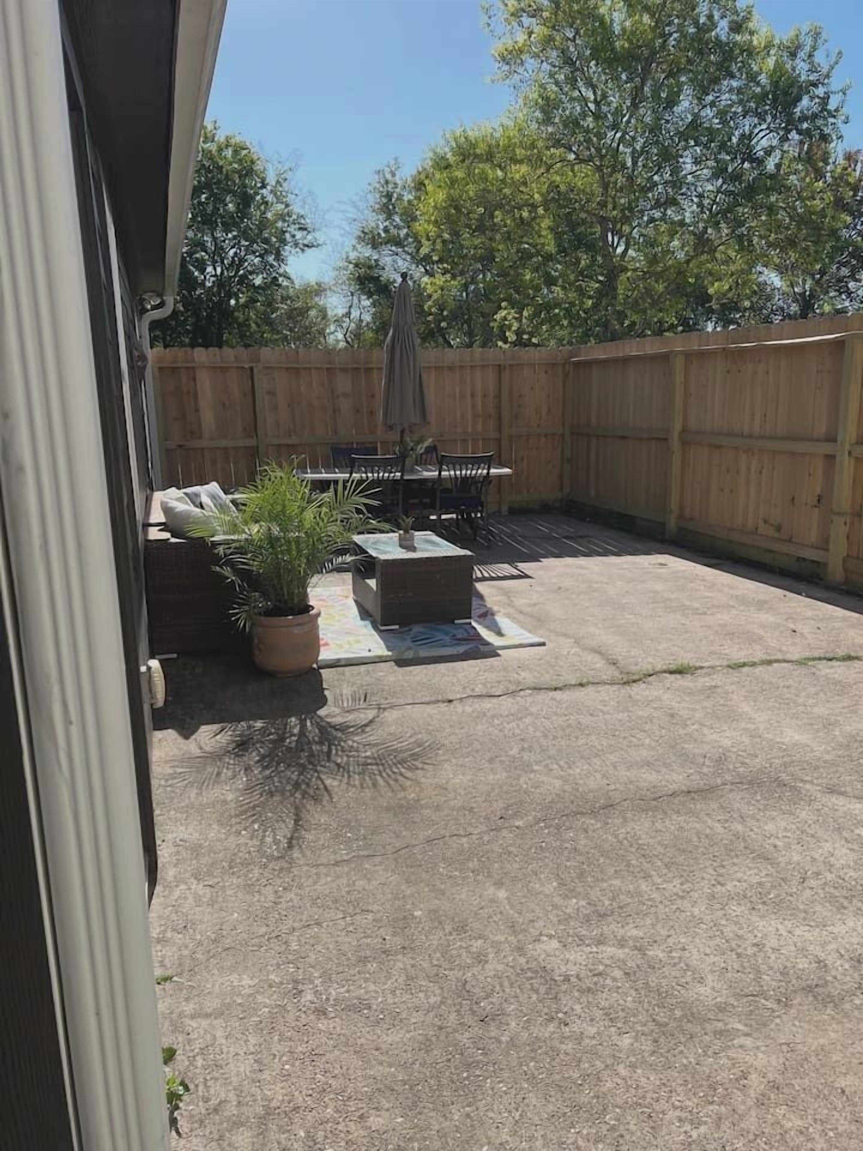 A backyard patio with a table and chairs, a wooden fence, and potted plants.