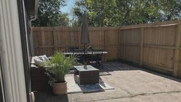 A backyard patio with a table and chairs, a wooden fence, and potted plants.