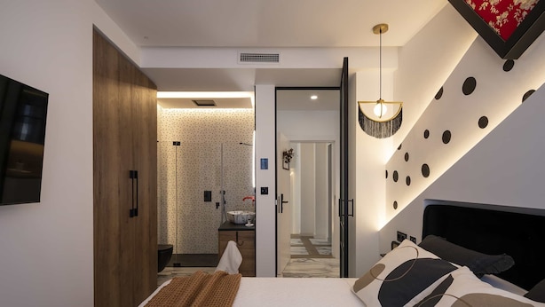 Une chambre d’hôtel moderne dotée d’un grand lit, d’une armoire en bois, d’une salle de bain avec un miroir et d’un design de plafond original.