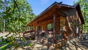 A wooden cabin with a porch, surrounded by trees. - 1 BR in Heart of Hochatown - 2 Min Walk to Putt-Putt (Broken Bow)