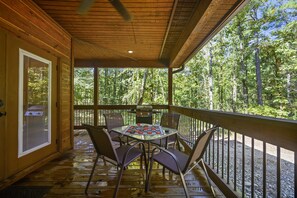 Um deck de madeira com mesa e cadeiras, com vista para uma área arborizada.