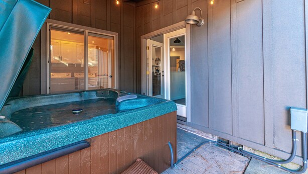 A hot tub with a wooden exterior, a glass door leading to a room, and a small outdoor area with a wooden deck. - Beautiful | Hot Tub | Pet Friendly | Fenced (Sisters)