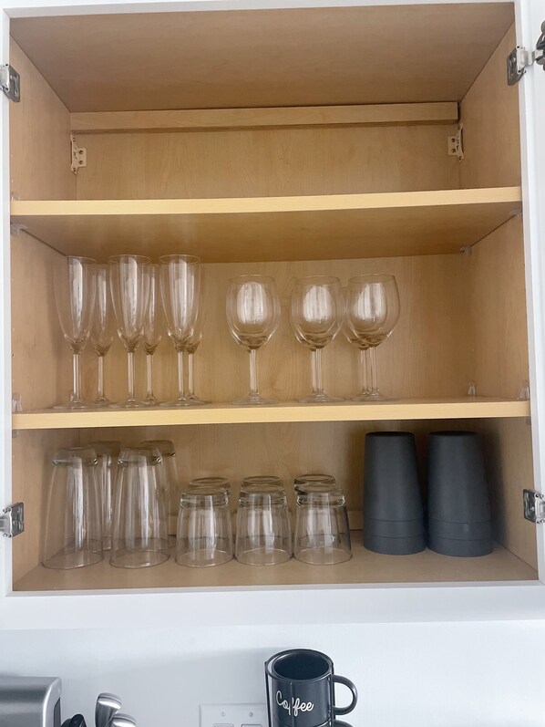 A cabinet with three shelves, each holding various glassware and mugs.