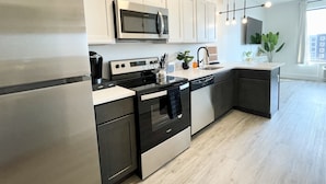 Una cocina moderna con electrodomésticos de acero inoxidable, armarios blancos y piso de madera.