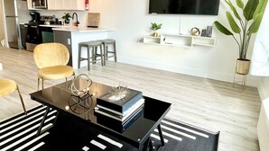 Una sala de estar moderna con una mesa de centro negra, un sofá y un televisor montado en la pared.
