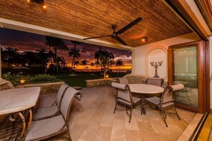 A patio area with a ceiling fan, a table and chairs, and a mural of a sunset over palm trees. - Palms 23 (The Palms)