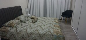 Quarto com cama, cadeira e janela com cortinas.