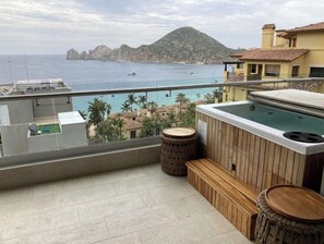 Enjoy breathtaking views of the sea and mountains from this balcony, featuring a hot tub and comfortable seating area.