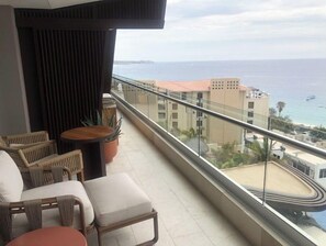 Enjoy the ocean view from this balcony with a sofa, chairs, and a table, surrounded by lush greenery.
