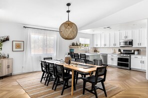 A modern kitchen with white cabinets, a central island, and a dining area with a wooden table and black chairs.