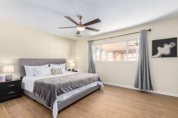 A bedroom with a bed, nightstands, a ceiling fan, a window with curtains, and a wall-mounted artwork. - 4b Tempe Beautiful backyard pool & firepit (Tempe)