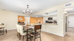 Una cocina moderna con electrodomésticos de acero inoxidable, un comedor con mesa y sillas de madera, y un jarrón decorativo sobre la mesa.