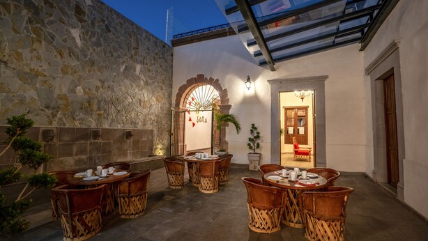 A courtyard with stone walls, a glass ceiling, and outdoor seating with tables and chairs. - Hotel Mesón de Sara (Querétaro)